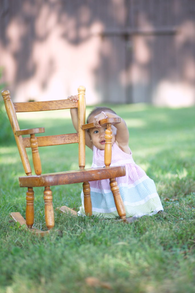 birthday girl peeks from behind rocking chair