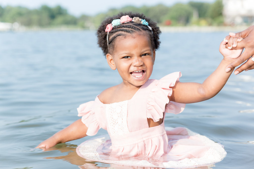 Two year old girl grins while wading in the water at a Pasadena, MD, beach.