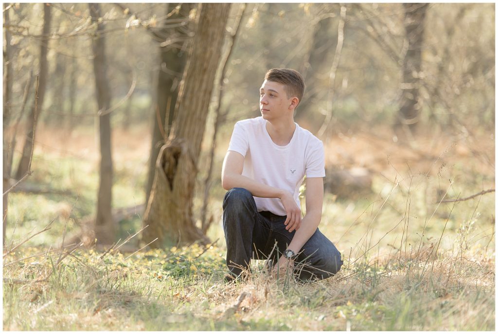Teen boy crouches in wooded area for senior session photos