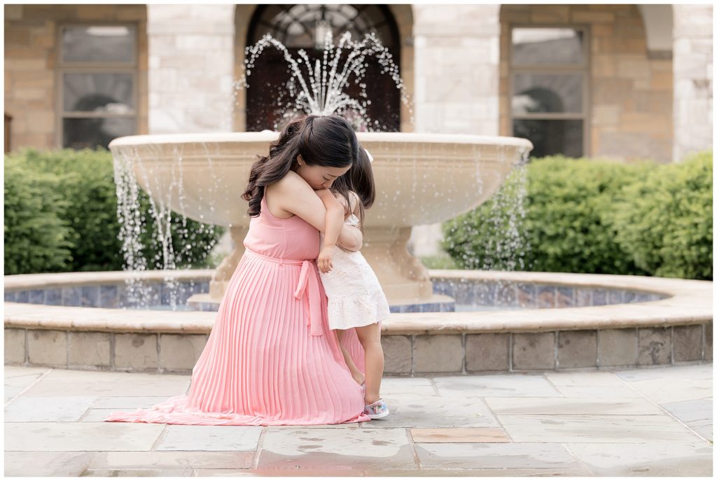 Mom hugs little girl in front of fountain