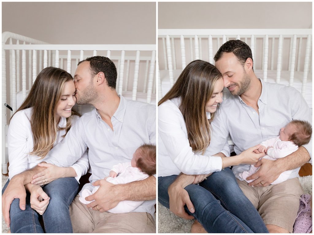 mom and dad sit against crib snuggling newborn and canoodling