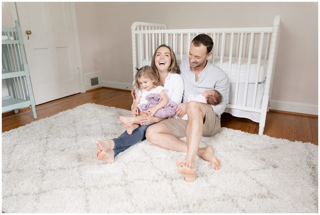 family sits on nursery floor laughing together