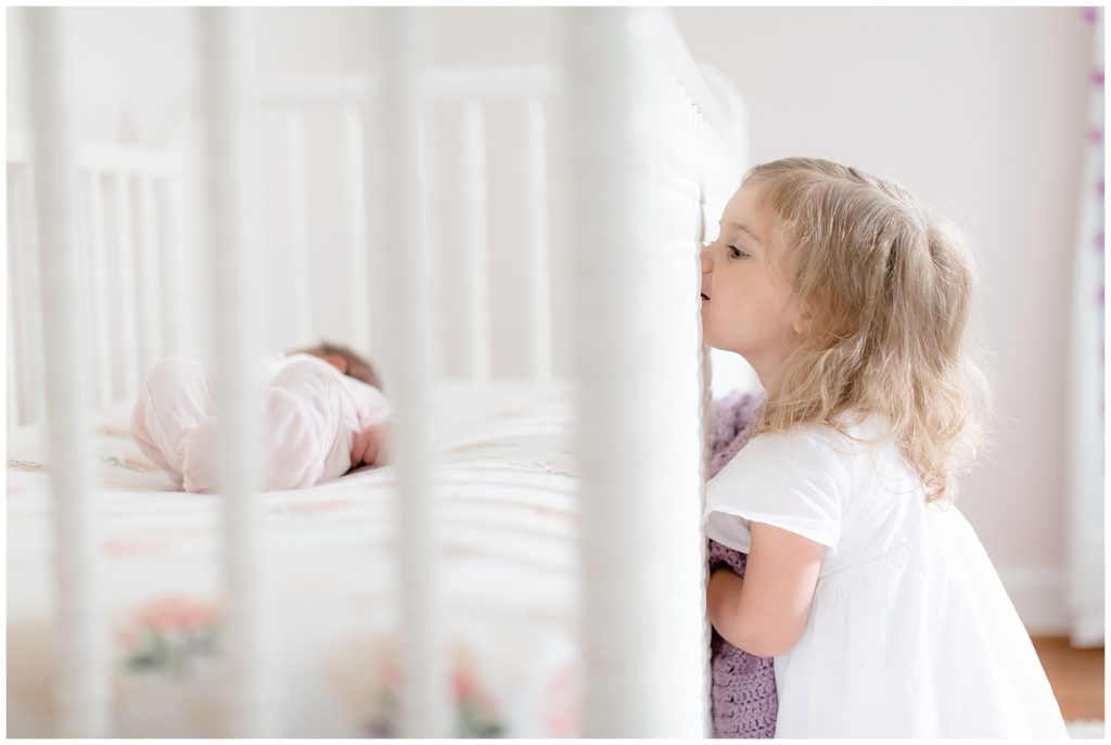 toddler sister peeks in the crib at newborn sister