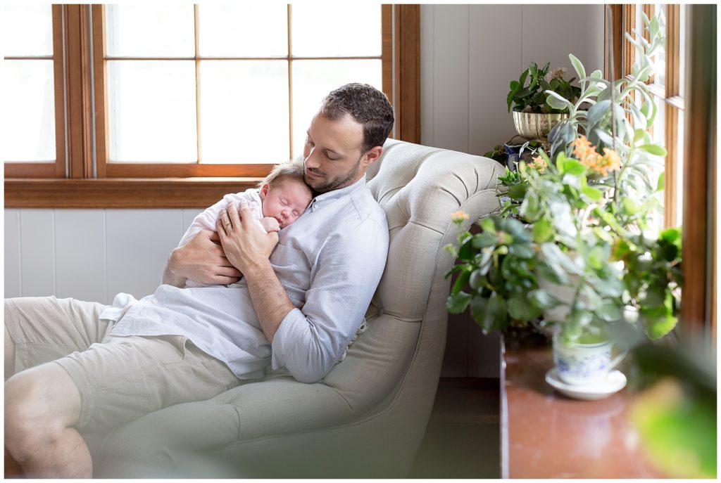 dad reclines in sunroom with new baby daughter
