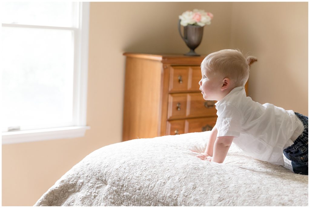 Toddler climbs on mom and dad's bed during lifestyle newborn session