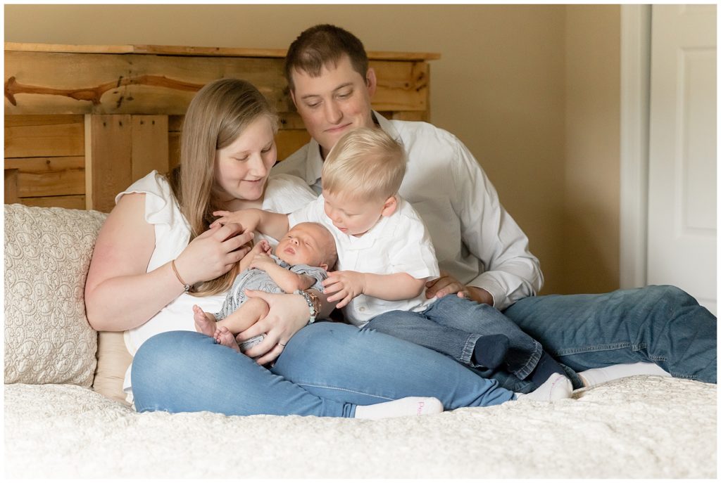Family of four sits on master bed during lifestyle newborn photos
