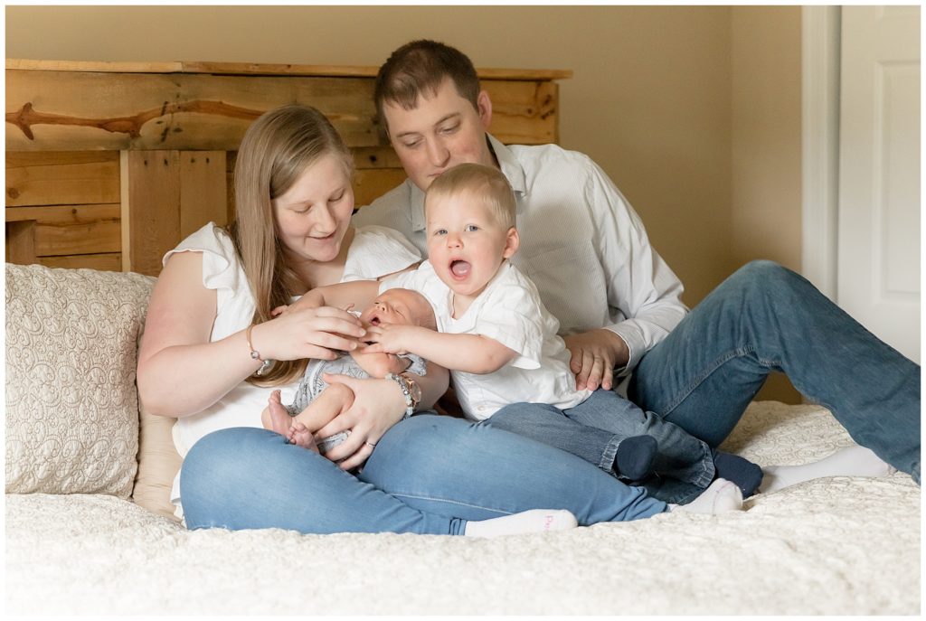 New family of four gathers for lifestyle newborn pictures on master bed