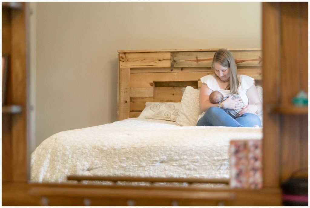 Shot in mirror of mom breastfeeding newborn son on master bed during lifestyle newborn session