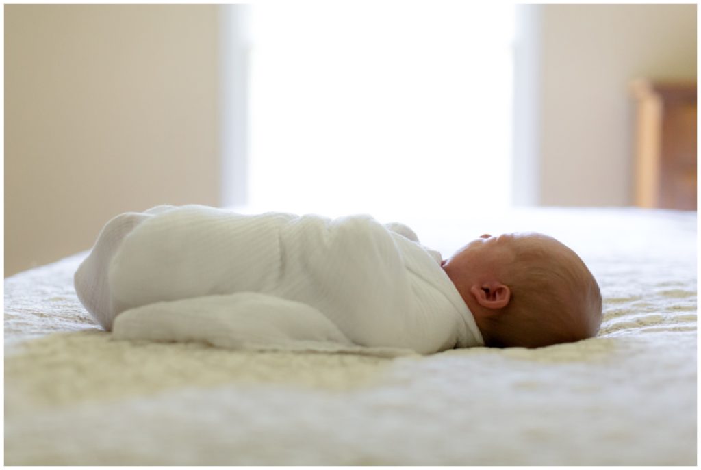 Swaddled newborn framed by window during lifestyle newborn session