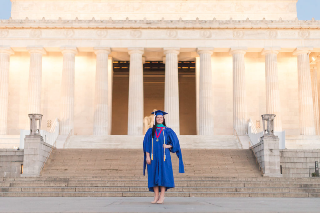 Woman in blue cap and gown stands in front of the Lincoln Memorial for her graduation photos.
