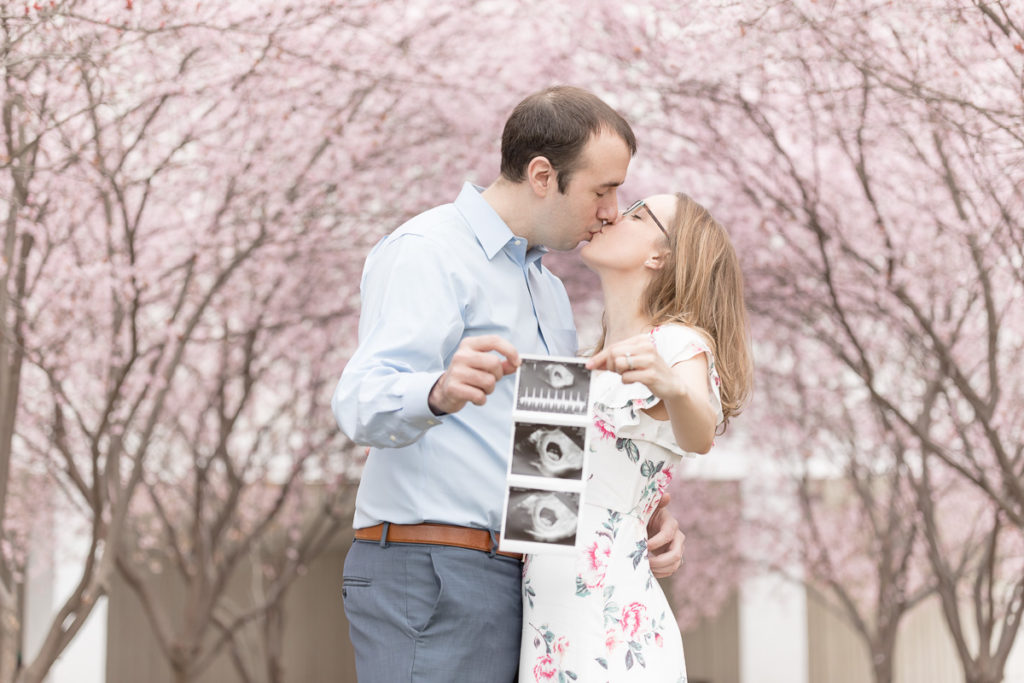 Expectant couple embrace while holding out ultrasound images to make a pregnancy announcment