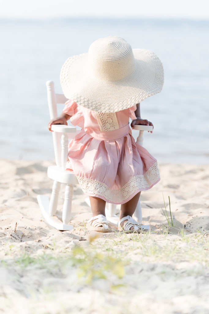 Two year old sits on a rocking chair with a sunhat covering her face.