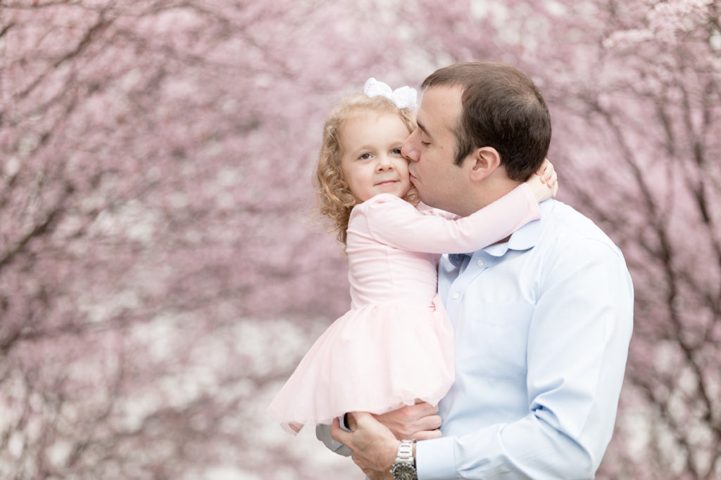 Dad kisses daughter in the shade of cherry blossom trees