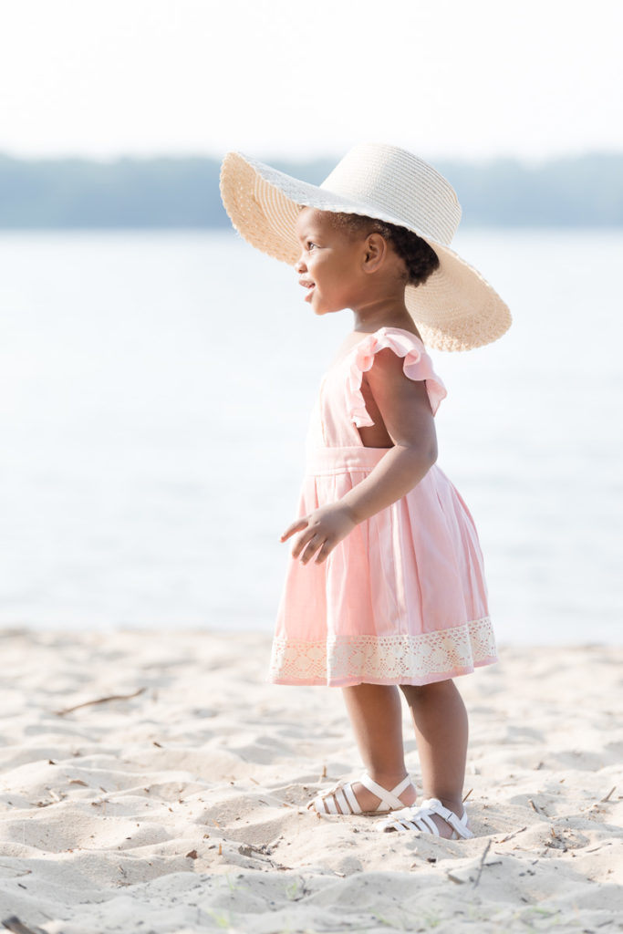 Toddler girl wears oversized beach hat for her two year milestone photos