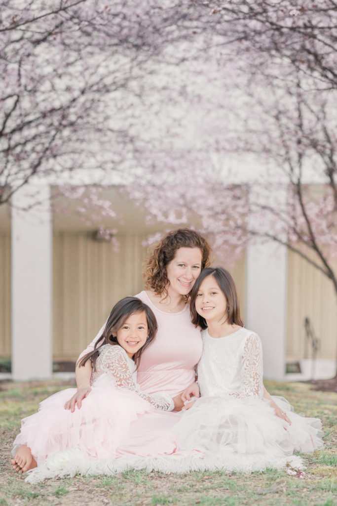 Mom and two daughters snuggle close on a blanket under cherry trees