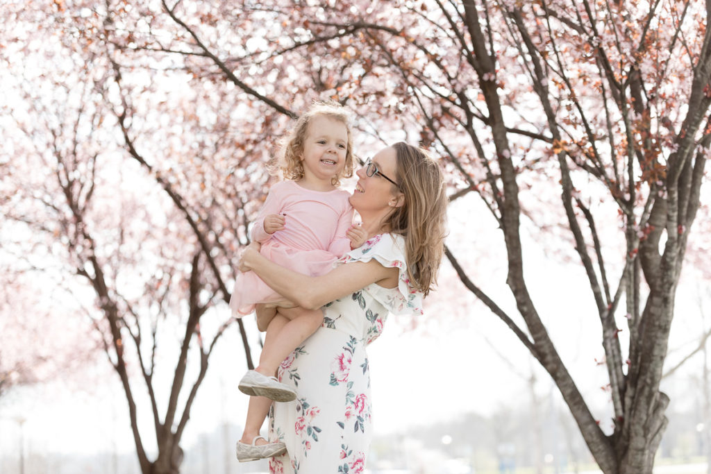 Mom snuggles daughter under blooming cherry blossoms