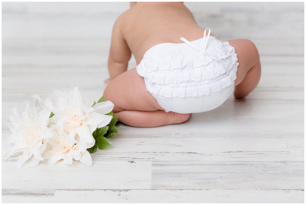 Baby girl in white bloomers crawls away from the camera