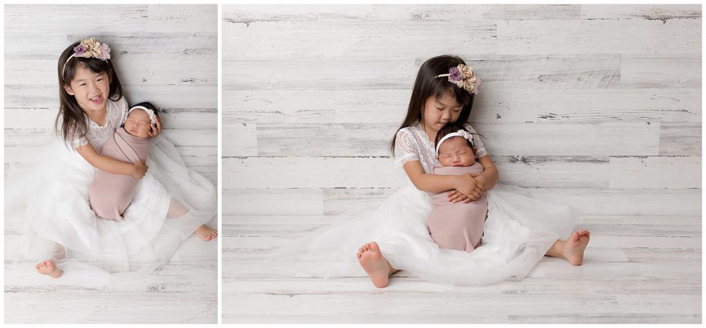 Big sister cuddles newborn baby during newborn photo session