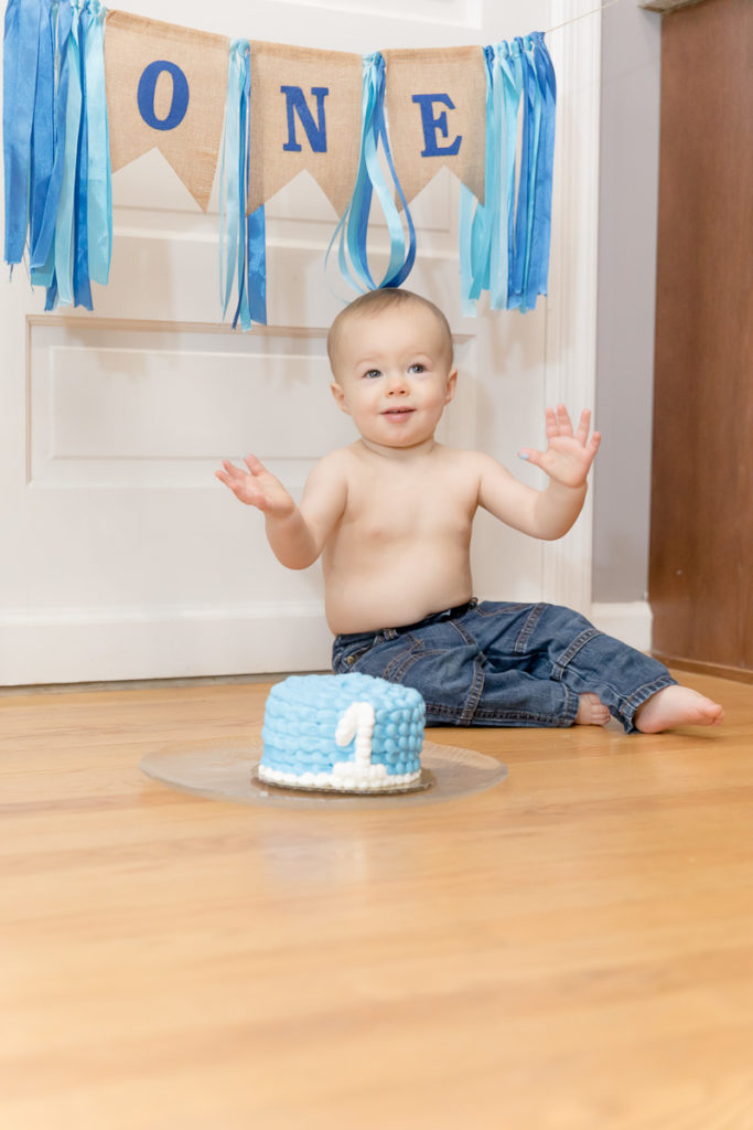 Baby sits with birthday streamer behind him and his hands in the air
