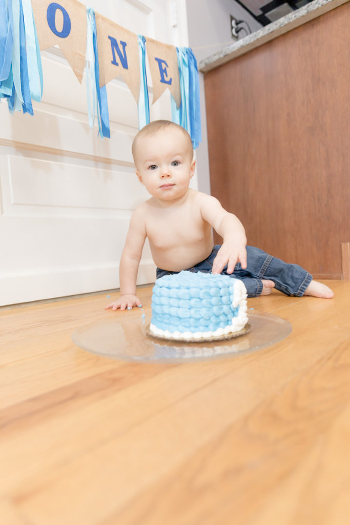 Baby peers at camera while touching blue birthday cake