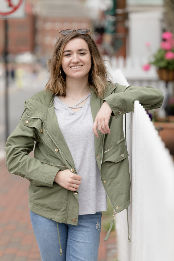 Girl leans against white fence in downtown Annapolis during senior portraits