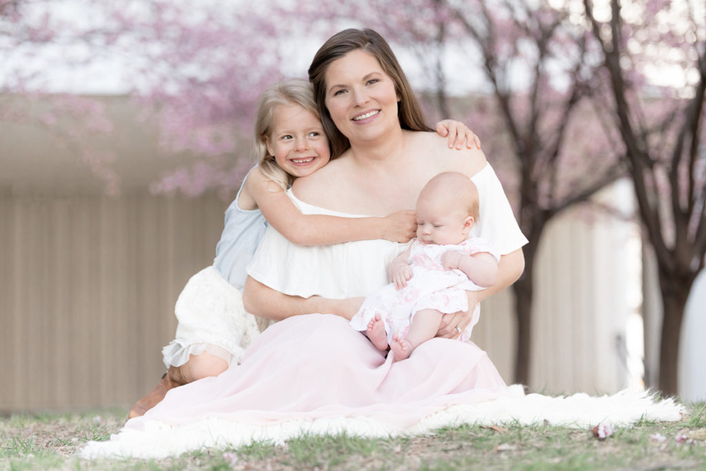 mom sits with daughters for cherry blossoms photos