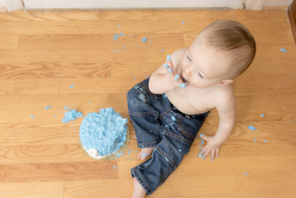 baby licks frosting off hands during one year cake smash