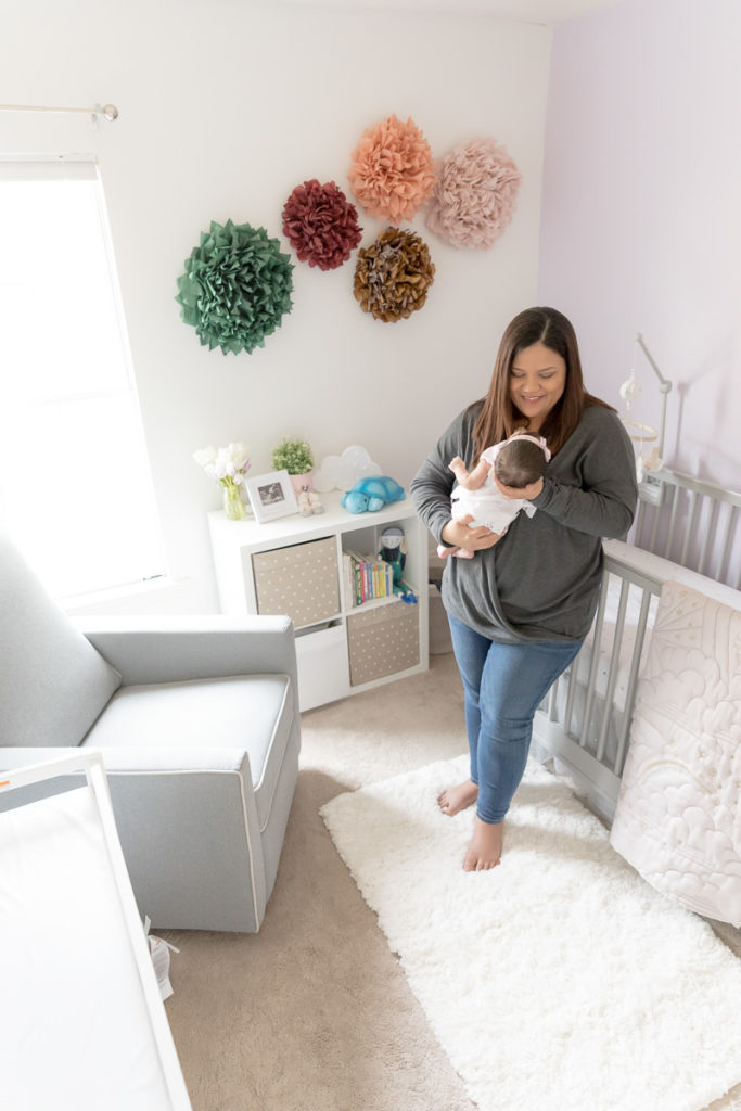 Mom stands in beautifully decorated nursery holding her new baby girl