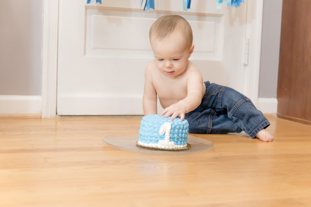 one year old boy touches his birthday cake