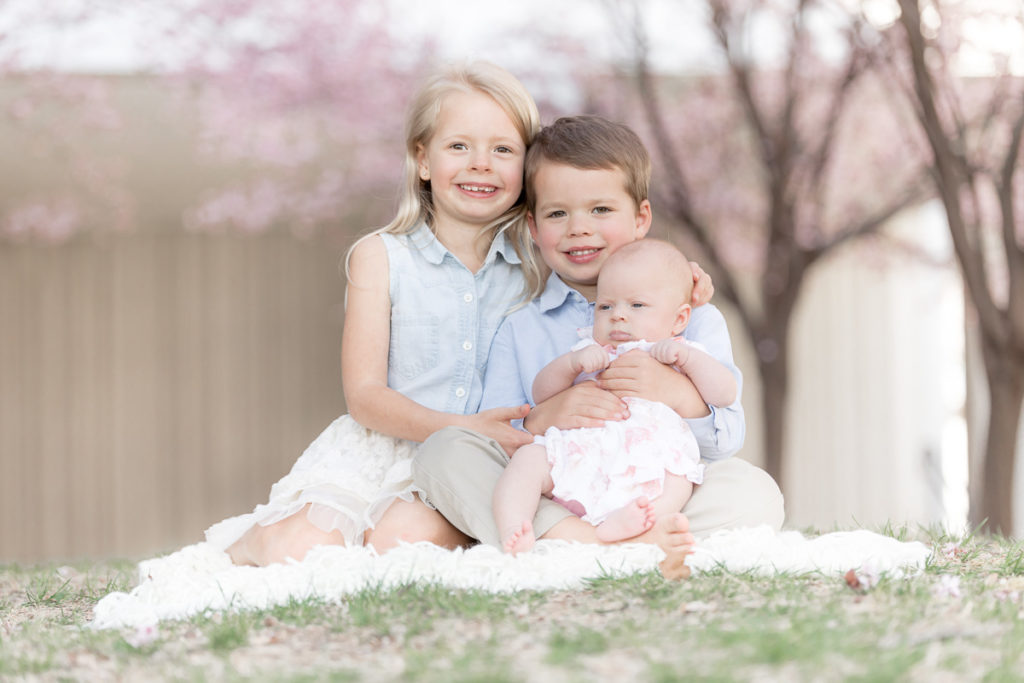 three beautiful children pose for photos on white blanket