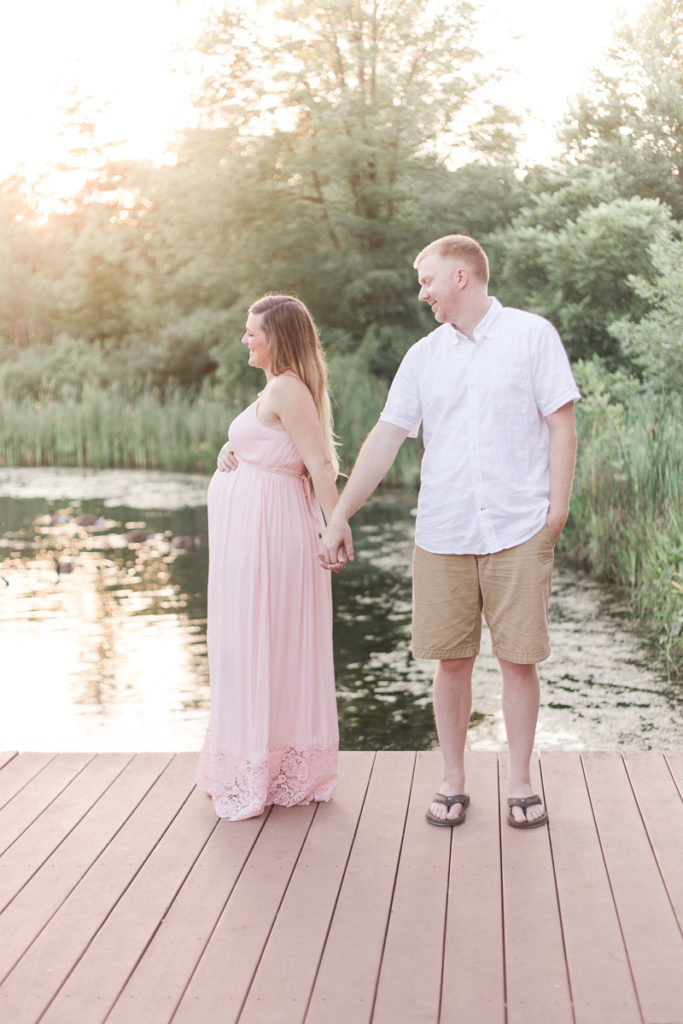 husband and pregnant wife hold hands in golden hour light