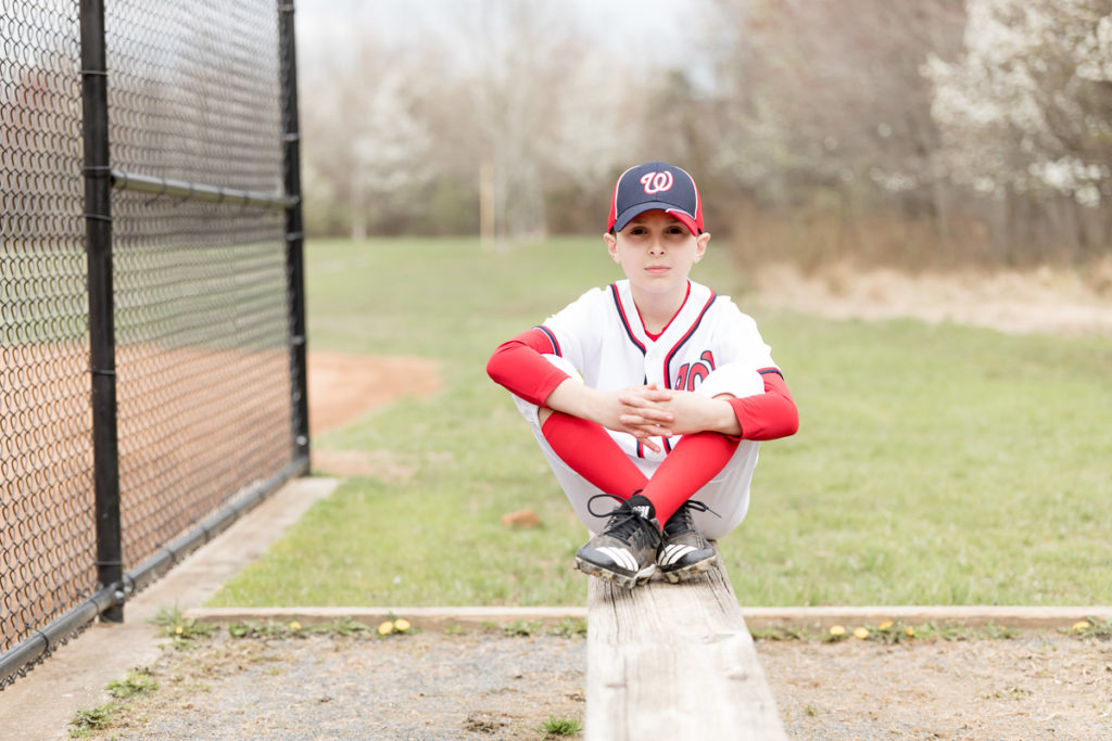 boy in baseball uniform poses on bench