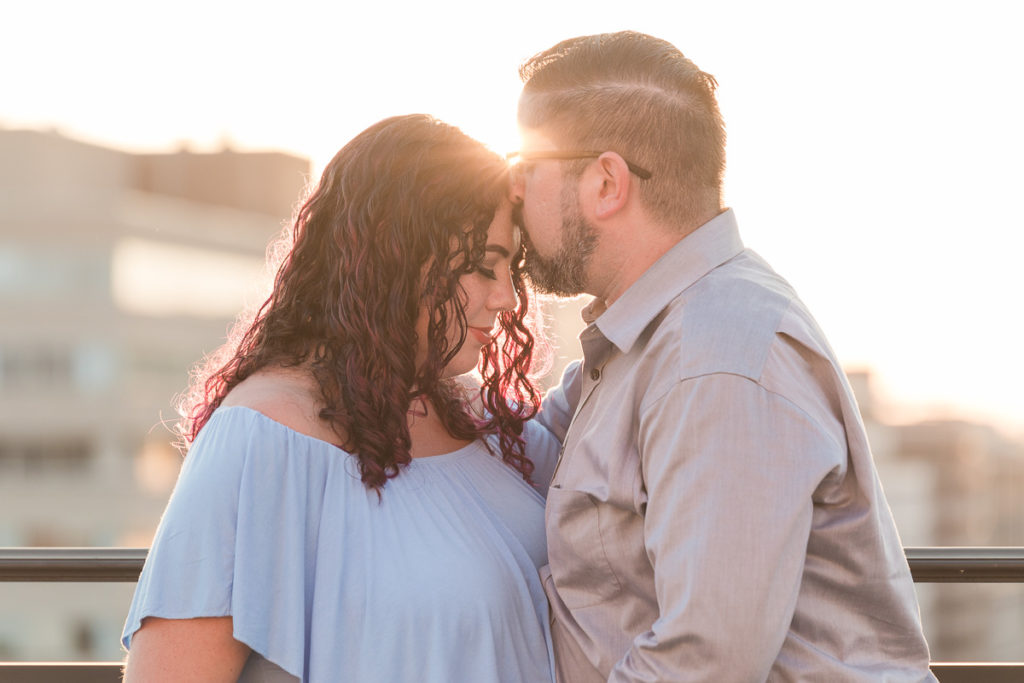 husband kisses wife's forehead in golden hour glow