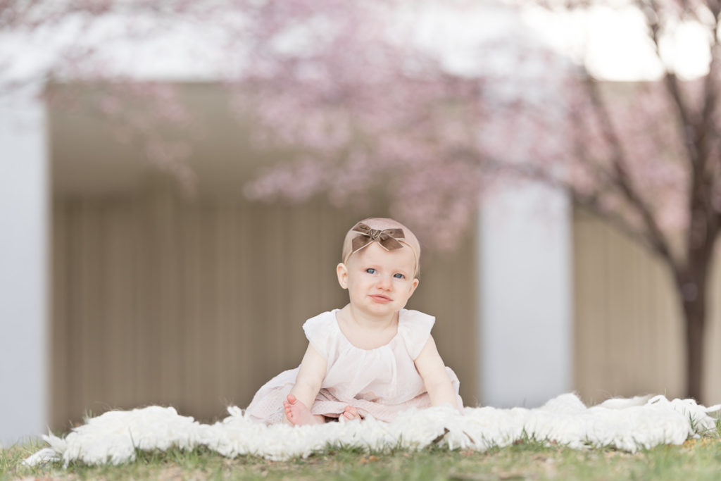baby sits on white blanket under flowering trees