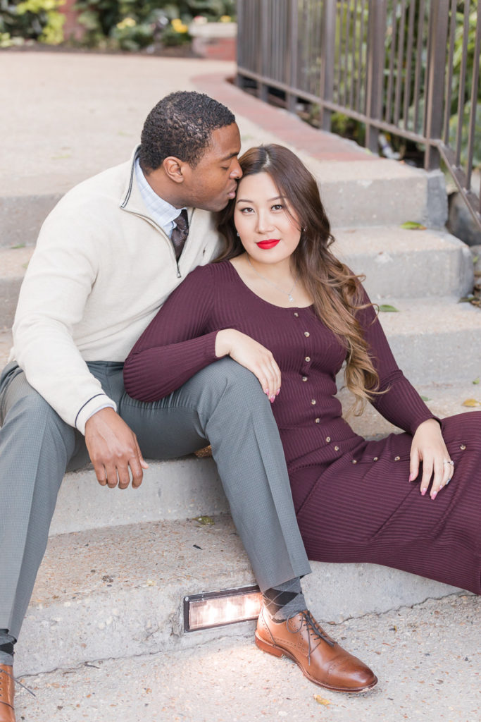 man kisses fiancee's temple while sitting on steps