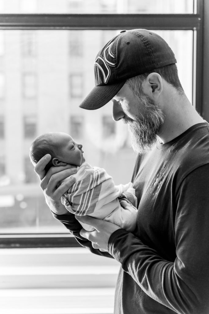 black and white image of dad and newborn standing in front of window