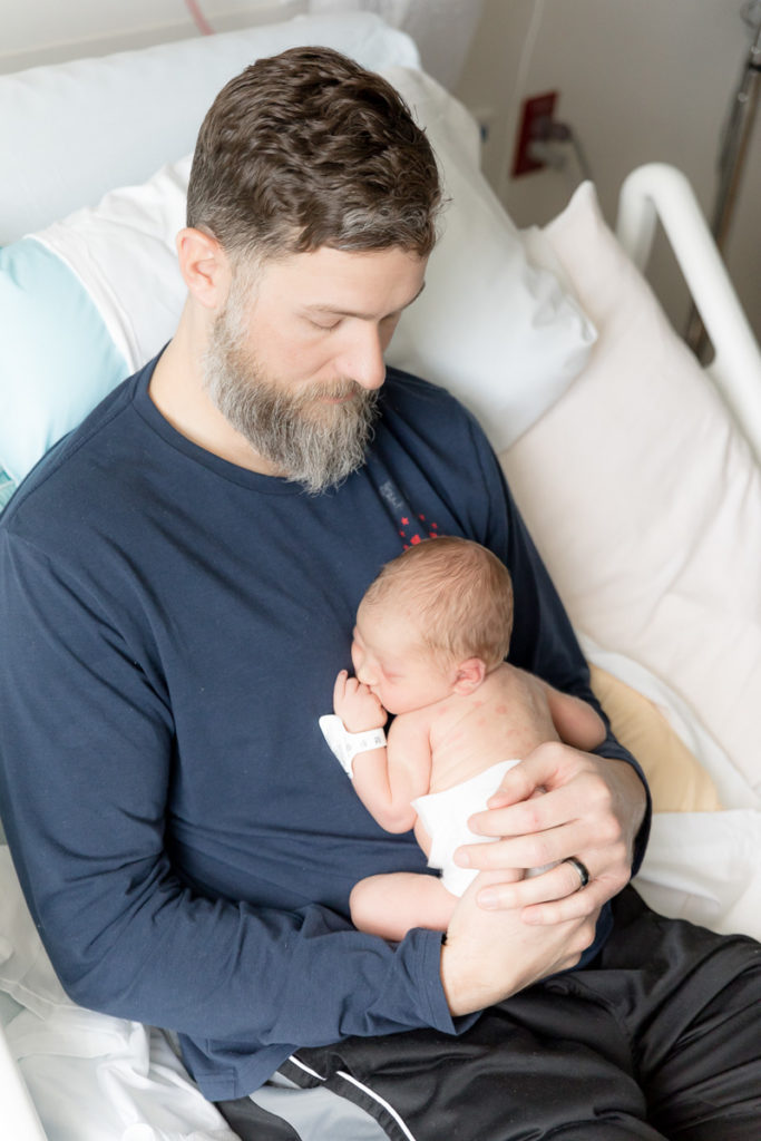 dad and newborn son sit in hospital bed