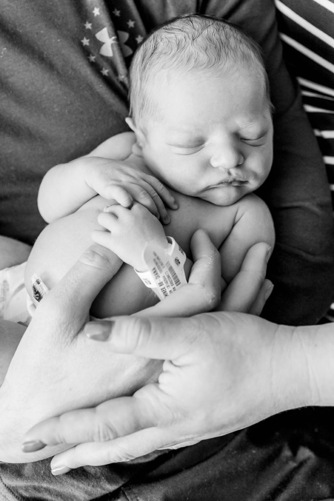 black and white shot of new baby with mom and dad hands