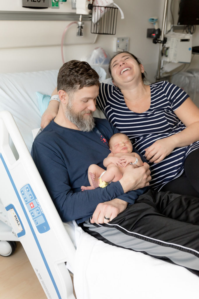 new parents laugh while sitting with newborn