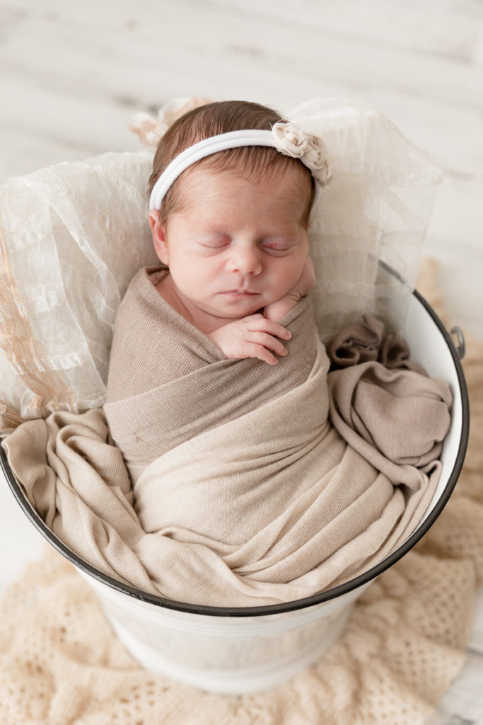 newborn in white bucket with headband and beige wrap