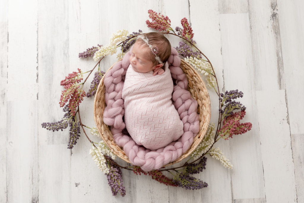 newborn in basket surrounded by flower garland