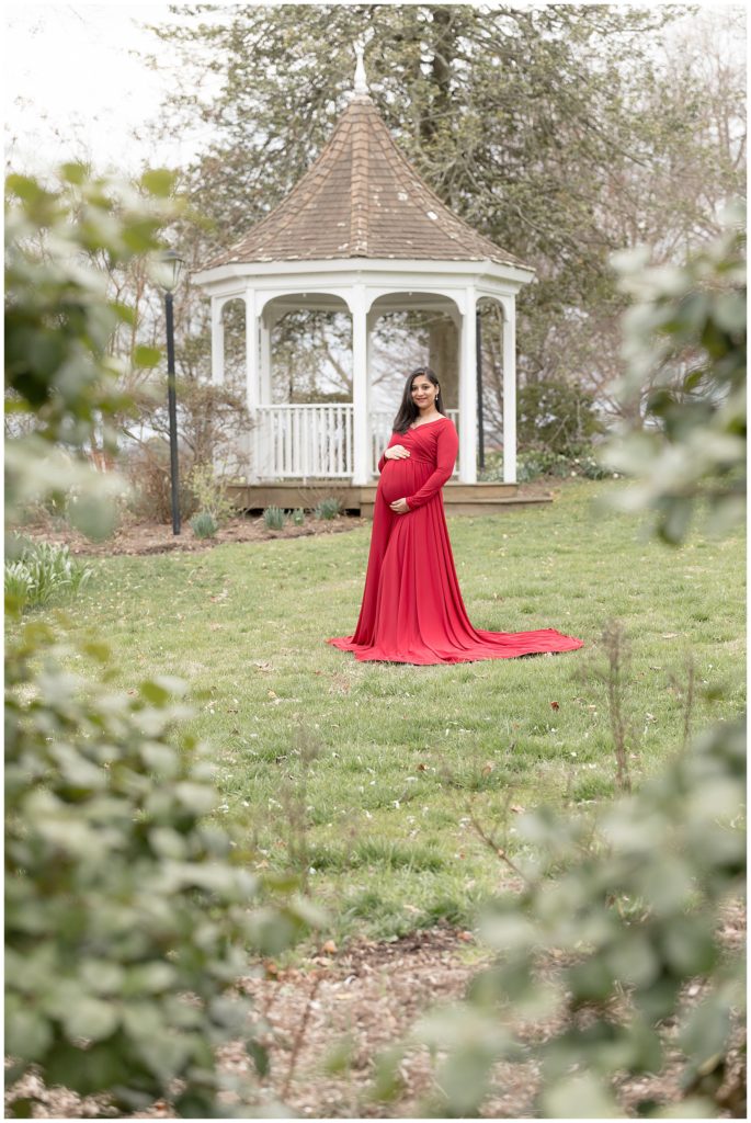 pregnant woman in Red Maternity Dress in front of white gazebo