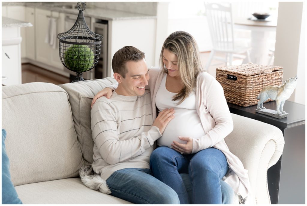 husband touches wife's pregnant tummy at home maternity photos