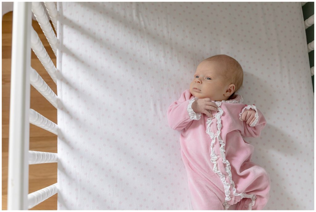 baby girl in pink lays in white crib