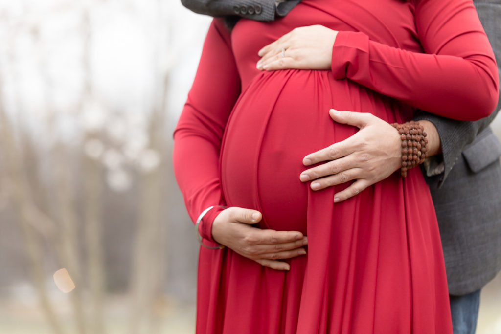 husband and wife hands on pregnant belly, red maternity dress
