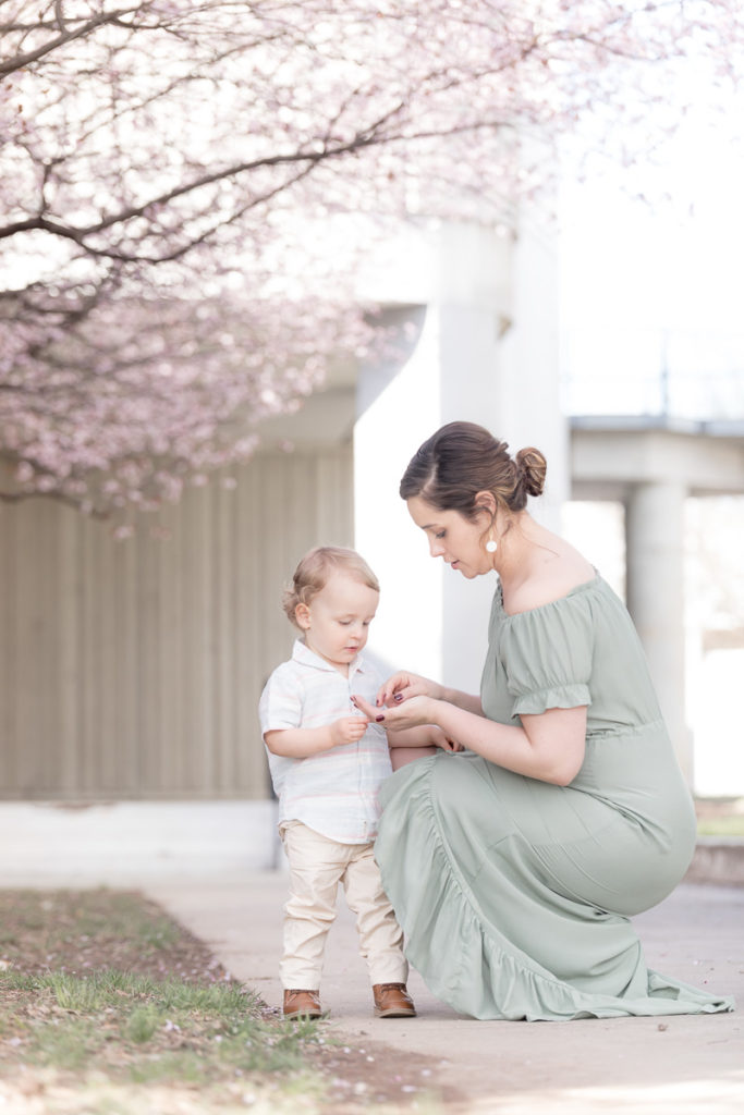 mom crouches to look at cherry blossom with son
