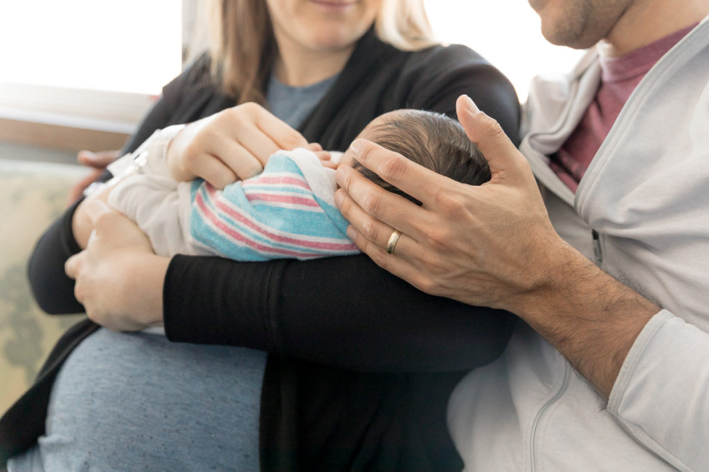 parent's hands against newborn baby