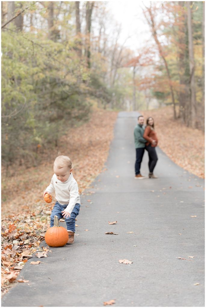 toddler plays with pumpkins while parents look on