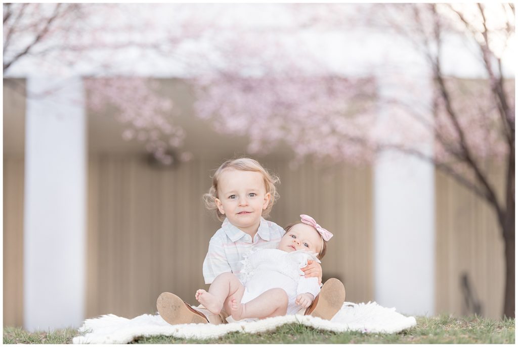 toddler holds baby sister under cherry blossoms