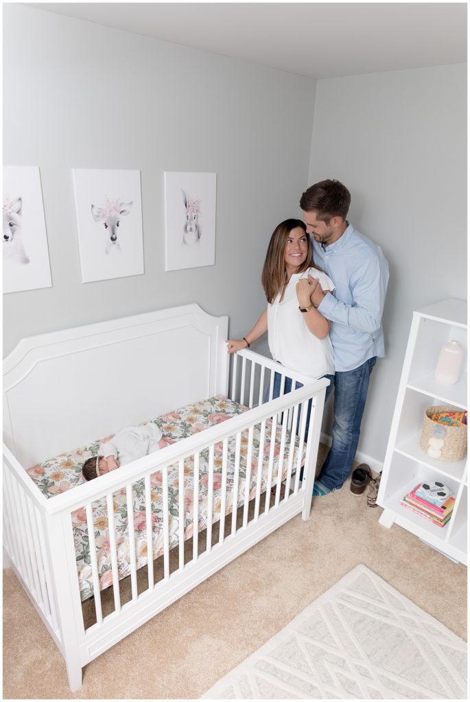 couple stand in nursery with newborn daughter